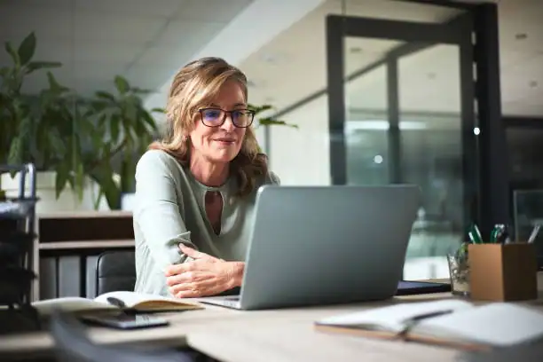 Senior woman using laptop at desk for tech support, remote learning, or online communication.